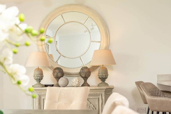 A room with a round mirror, two lamps, decorative vases, and a chair.