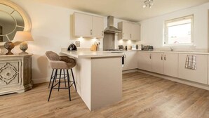 A modern kitchen with a central island, bar stools, and a large window. - Village Green | Kingsbarns (Kingsbarns)