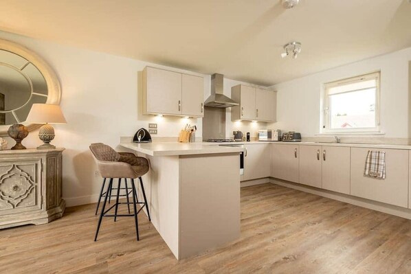 A modern kitchen with a central island, bar stools, and a large window.