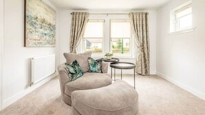 A cozy living room with a beige sofa, a round coffee table, and patterned curtains. - Village Green | Kingsbarns (Kingsbarns)