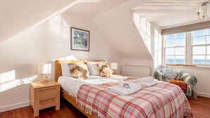 Ein Schlafzimmer mit einem hölzernen Bett, einer karierten Decke, einem Nachttisch, einem Fenster mit Blick und einem Gemälde an der Wand.