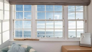 Ein Zimmer mit großem Fenster mit Meerblick, einem Bett mit gestreifter Decke und einer Holzkommode.