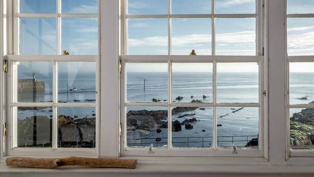 Ein großes Fenster mit vielen Scheiben, das Blick auf das Meer und die felsige Küste bietet.