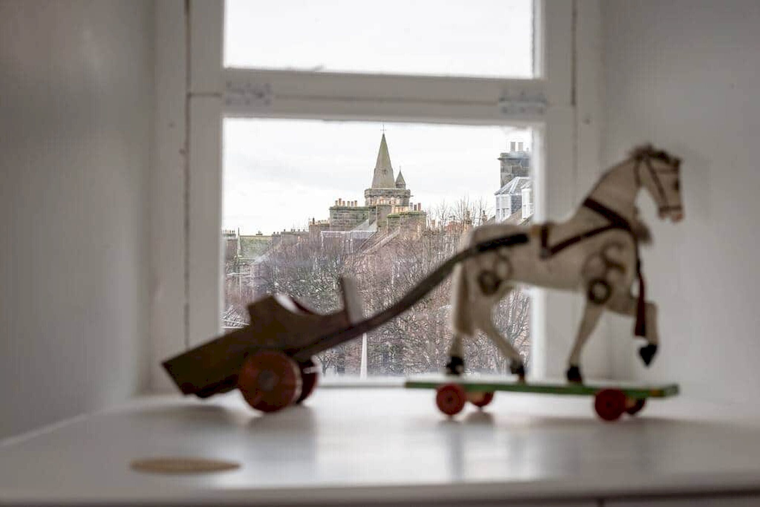 Ein Spielzeugpferd auf einem Regal mit Blick aus dem Fenster auf eine Stadtansicht.