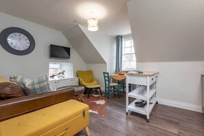 Een gezellig compact woongedeelte met een bank, een eettafel, een televisie en een kleine keuken met een karretje.