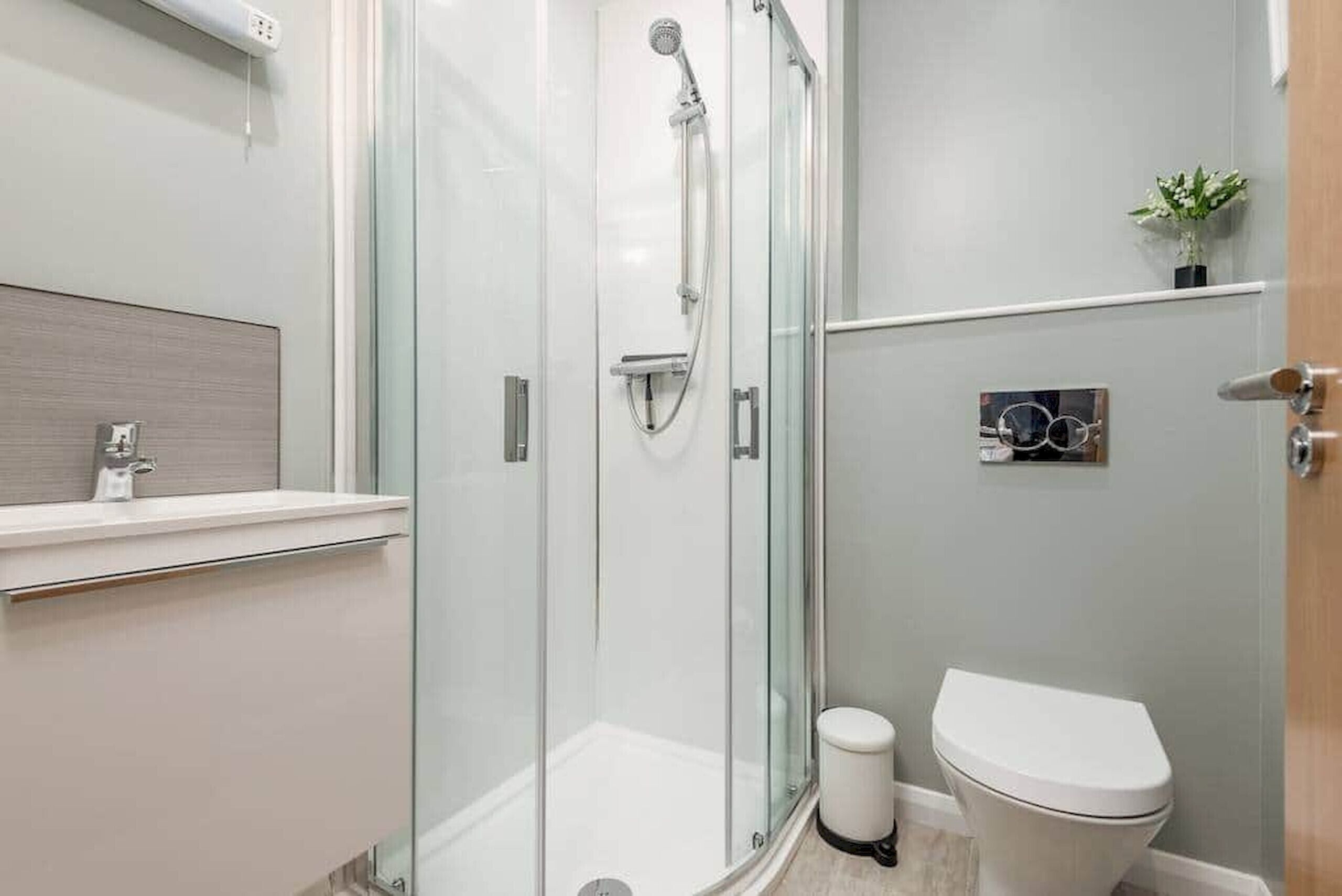 A modern bathroom with a glass-enclosed shower, a toilet, and a small sink.