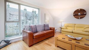 A living room with a brown leather sofa, a yellow sofa, a wooden coffee table, and a round wooden clock on the wall.