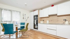 A modern kitchen with white cabinets, a wooden countertop, and a dining area with teal chairs.