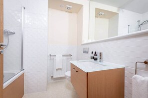 Un baño moderno con cabina de ducha de vidrio, un lavamanos blanco con tocador de madera y un espejo grande sobre el tocador.