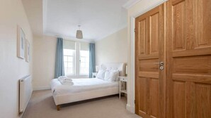 Une chambre à coucher avec un lit, une table de chevet, une armoire en bois et une fenêtre avec des rideaux.