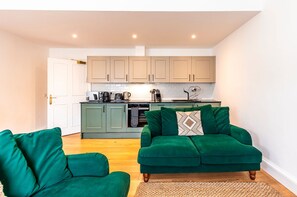 Ein modernes Wohnzimmer mit einer grünen Sofagarnitur und einer Küche im Hintergrund.