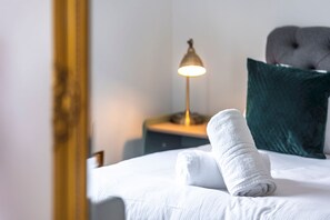 Un lit bien fait, avec une serviette blanche, une lampe de chevet et un oreiller vert.