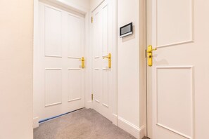 Un couloir avec des portes blanches, dont certaines ont des poignées jaunes, et un petit écran fixé sur l’une des portes.