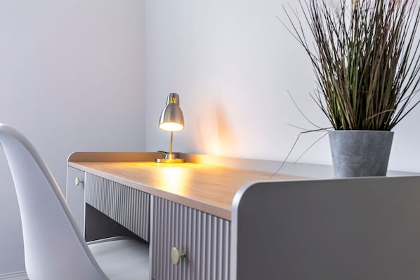 A modern desk with a lamp, a potted plant, and a chair.