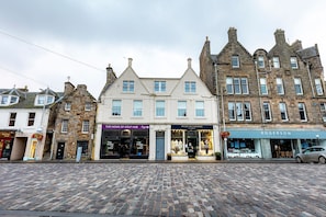 Une rue pavée bordée de bâtiments historiques, dont une boutique dont l’enseigne indique « The Home of Golf » et une autre, « House of Cashmere ».