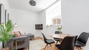 Una sala de estar moderna con un sofá gris, sillas negras, una mesa de comedor de madera y un televisor montado en la pared.
