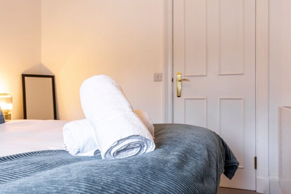 A neatly made bed with a rolled white towel and a grey bedspread in a hotel room.