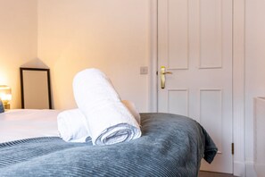 A neatly made bed with a rolled white towel and a grey bedspread in a hotel room. - Skye Sands | Eden Residence (St Andrews)