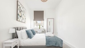 Un dormitorio moderno con cama, mesita de noche y ventana con vistas a edificios.