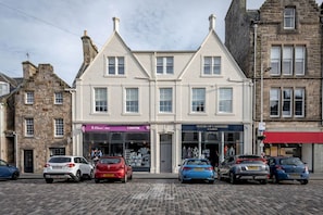 A row of parked cars in front of a building with shops on the ground floor.