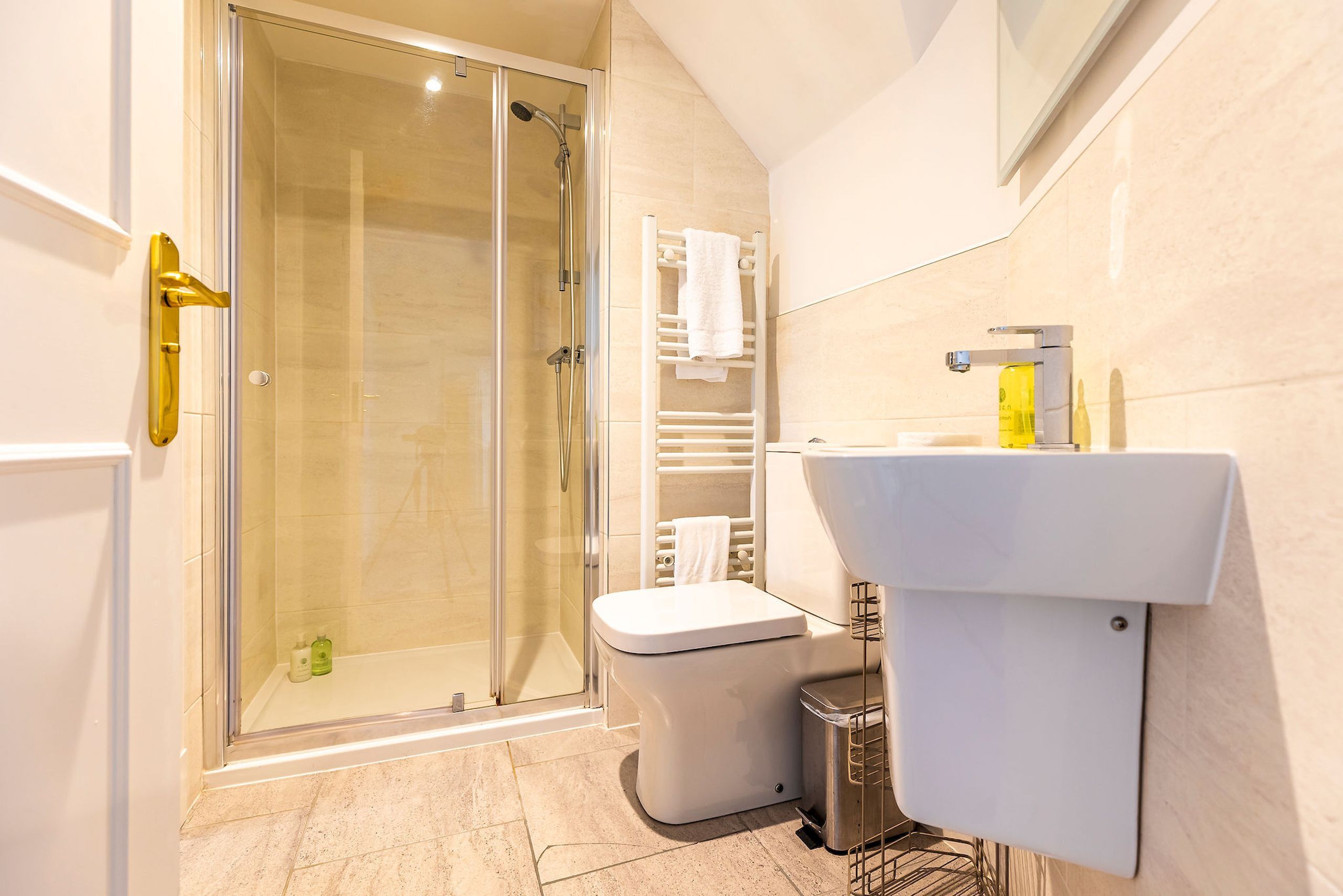 A modern bathroom with a glass-enclosed shower, a white toilet, and a sink with a yellow soap dispenser.