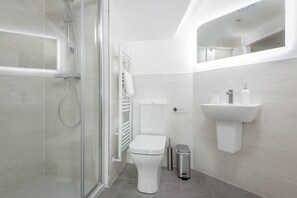 Une salle de bain moderne avec une douche à parois de verre, des toilettes blanches, un lavabo fixé au mur et une poubelle.