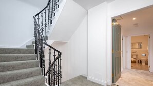 A staircase with a grey carpet and black balusters, leading to a bathroom with a white toilet and a mirror. - Skye Sands | Balgove Penthouse Residence (St Andrews)