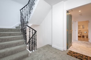 A staircase with a grey carpet and black balusters, leading to a bathroom with a white toilet and a mirror.