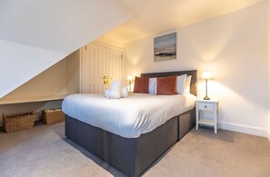 A bedroom with a bed, two bedside lamps, a nightstand, a painting on the wall, and a door with a handle.