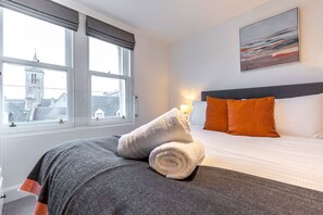 A hotel room with a bed, a window with a view of a tower, and a painting on the wall.