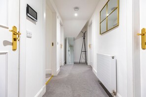 A hallway with white walls, a grey carpet, a white radiator, and a black tripod.