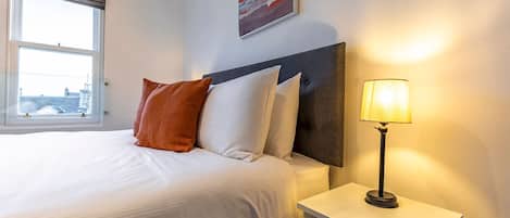Una habitación de hotel con una cama, una mesita de noche, una lámpara y una ventana.