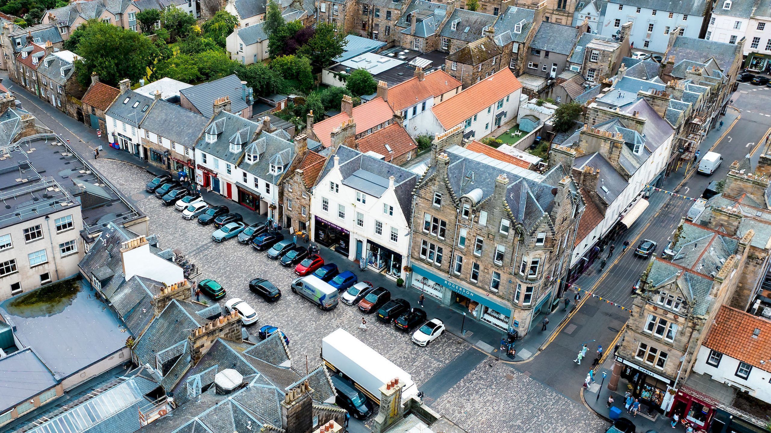 An urban street with historic buildings, a parking lot, and a pedestrian walkway.