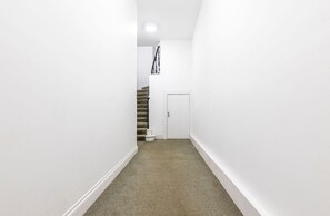 A narrow hallway with a carpeted floor, white walls, and a door at the end.