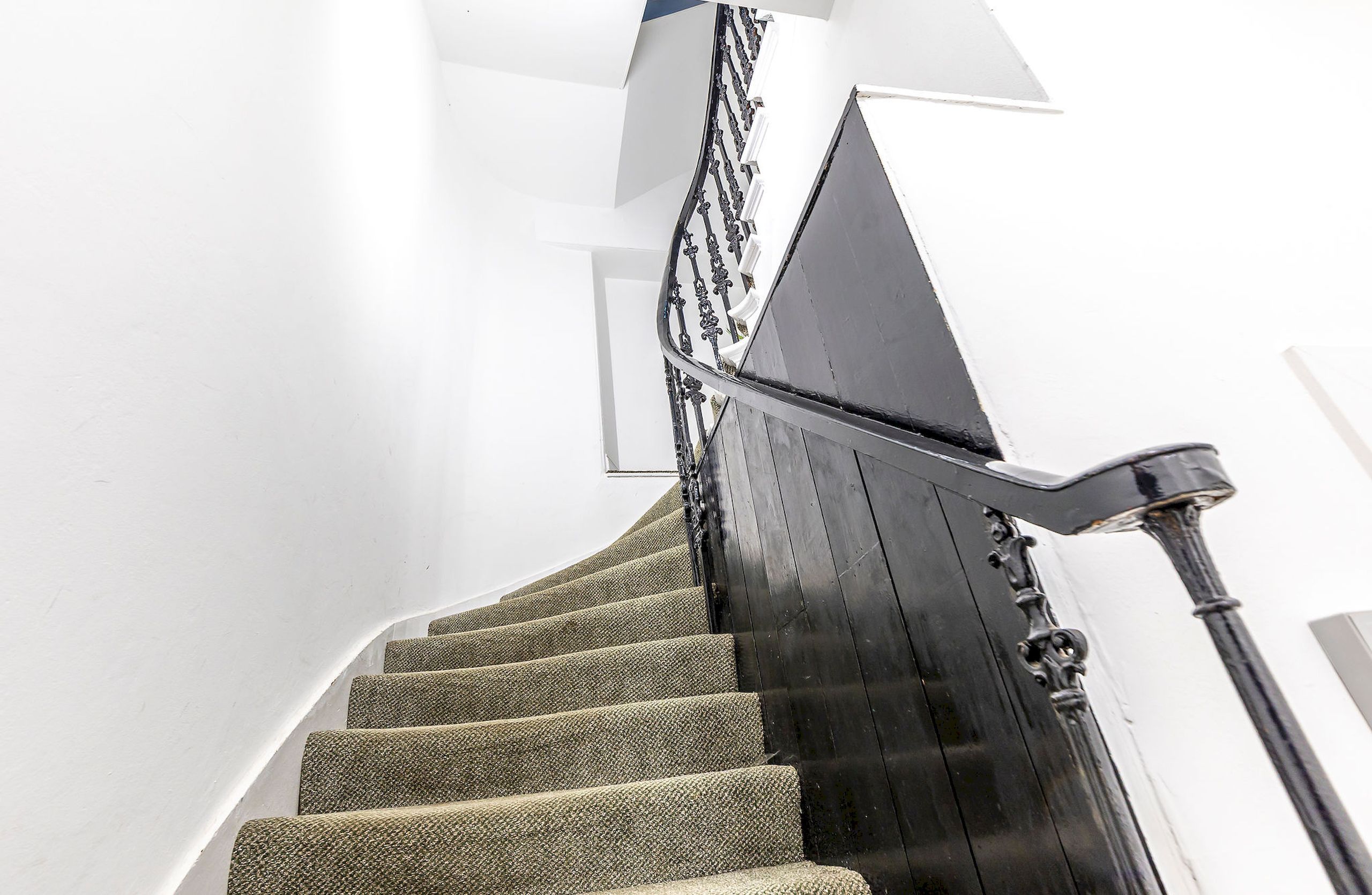 A spiral staircase with carpeted steps and a black handrail.