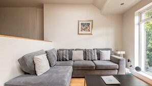 Uma sala de estar moderna com um sofá seccional cinza, uma mesa de centro de madeira e um quadro pendurado na parede.