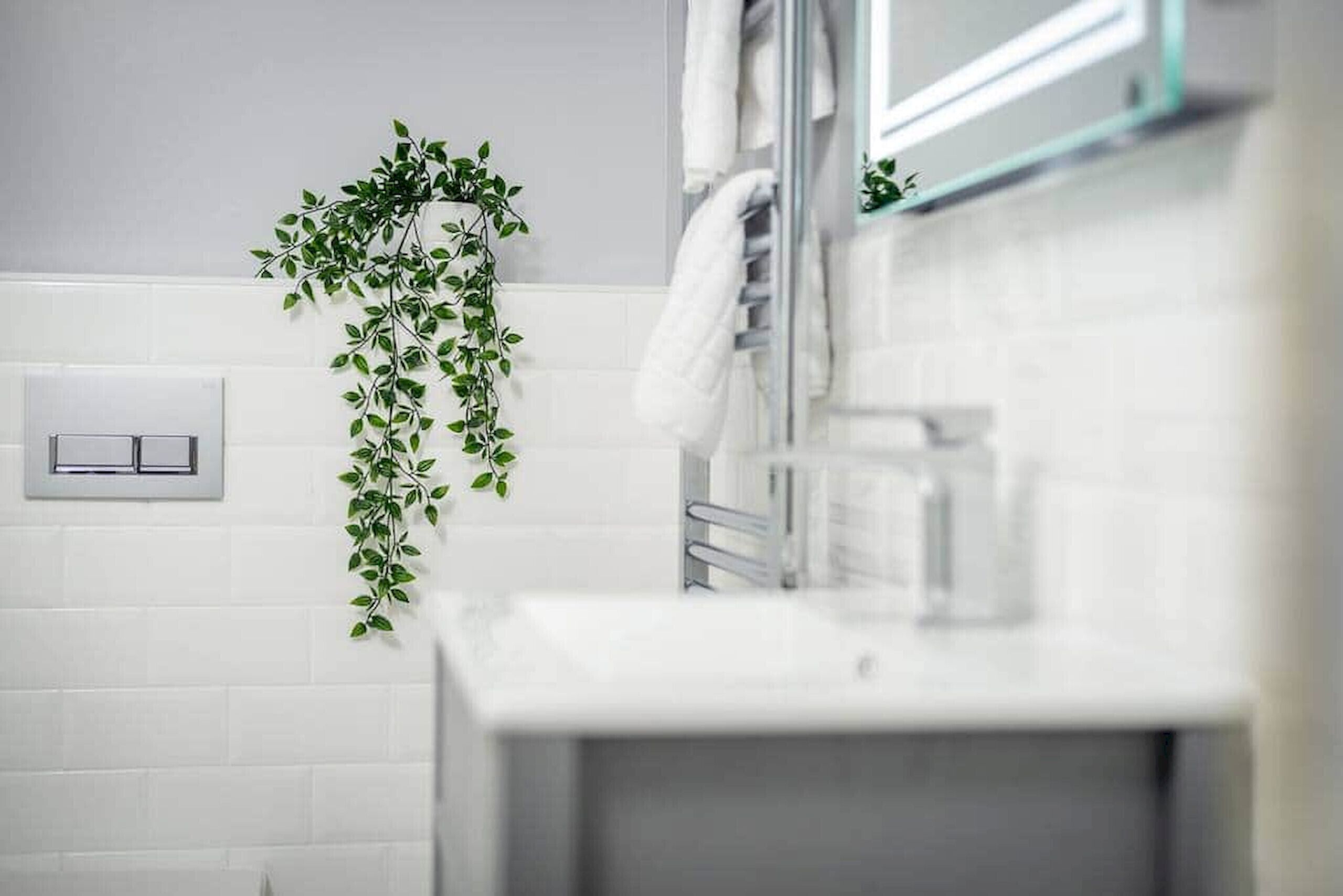 Een badkamer met witte tegels, een handdoekhouder, een plant en een spiegel.