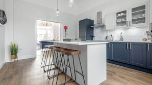 A modern kitchen with a central island, bar stools, and dark cabinetry. - Skye Sands | Alexandra Penthouse (No 8) (St Andrews)