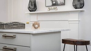 A kitchen with a white countertop, a basket, a decorative bull head, a framed animal picture, and two black vases. - Skye Sands | Alexandra Penthouse (No 8) (St Andrews)