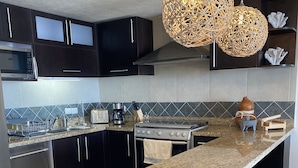 A modern kitchen with dark cabinets, a granite countertop, a stainless steel stove, and a unique woven light fixture.