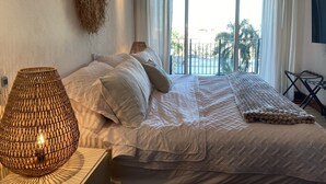 A bedroom with a large bed, a hanging plant, and a view of the outdoors.