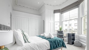 Ein modernes Schlafzimmer mit einem großen Bett, einem Schreibtisch und Blick auf die Stadt durch große Fenster.
