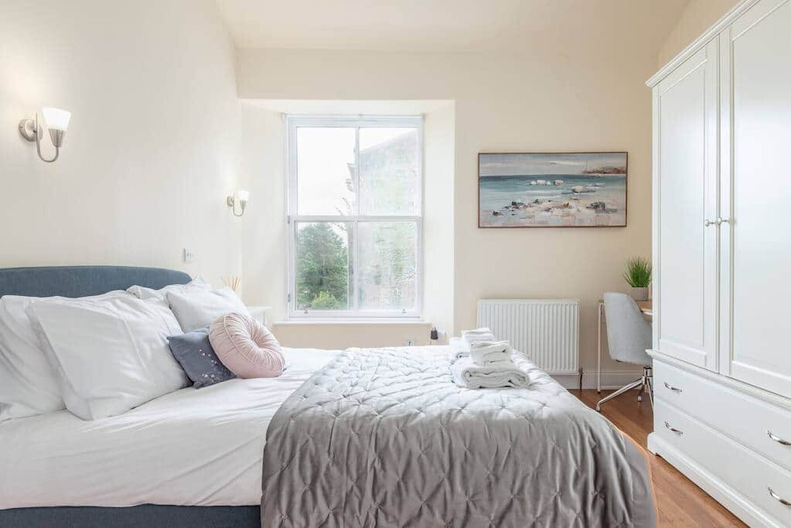 Een slaapkamer met een bed, raam, radiator, bureau en kast.