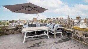 Un área de estar al aire libre con una mesa, un sofá, una sombrilla y vistas a edificios históricos.