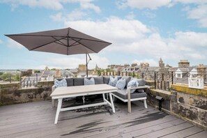 Et udendørs opholdsområde med et bord, en sofa, en parasol og udsigt til historiske bygninger.