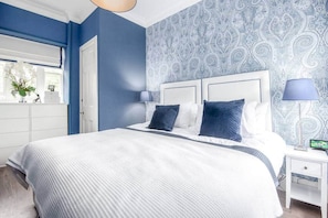Une chambre à coucher avec un grand lit, deux lampes de chevet, une table de nuit et une fenêtre donnant sur l’extérieur.