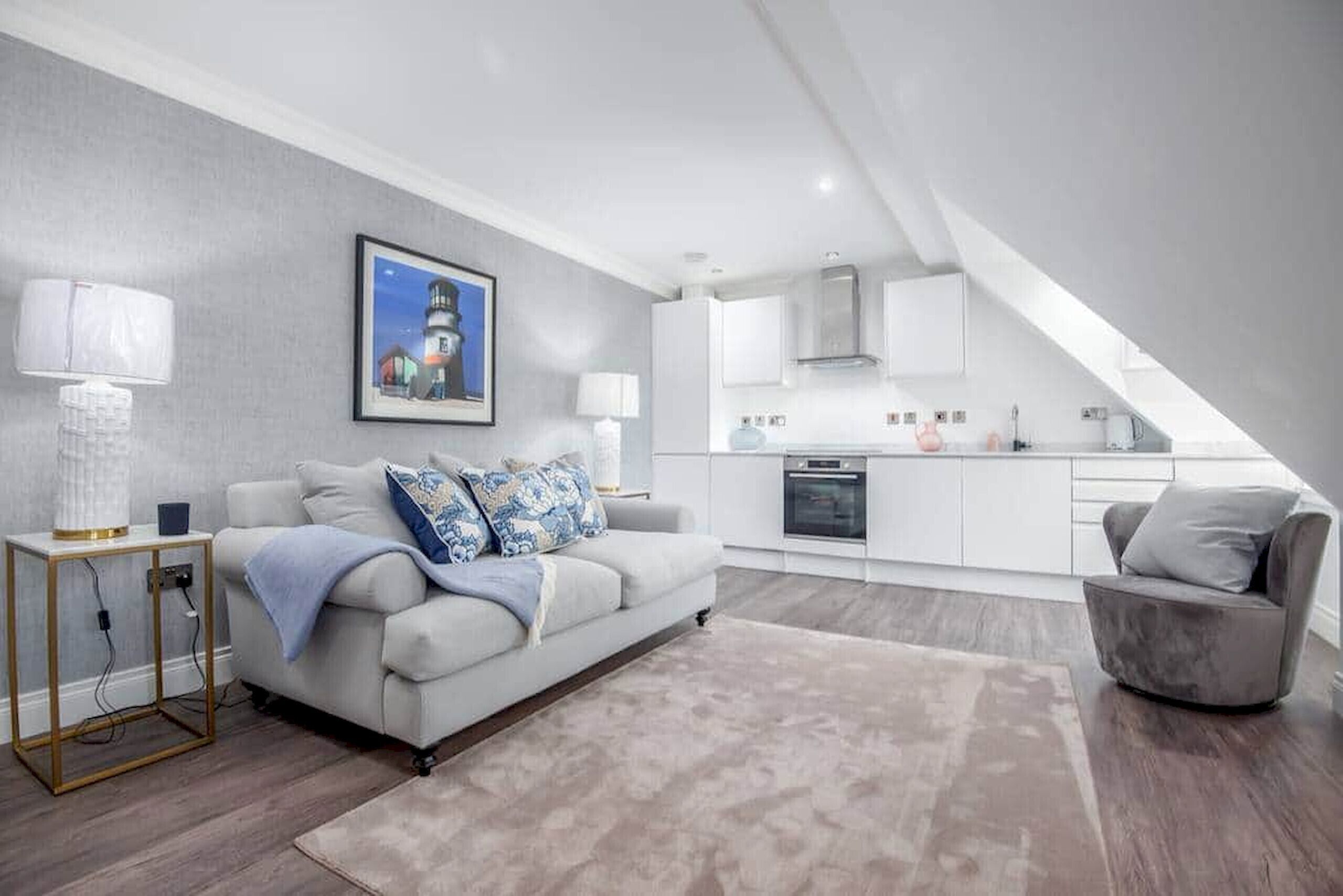 A modern living room with a sofa, a coffee table, and a rug. There is a kitchen area with cabinets and a stove.
