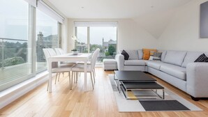 Un salon moderne comprenant un coin repas, de grandes fenêtres, un canapé gris et une table basse noire.