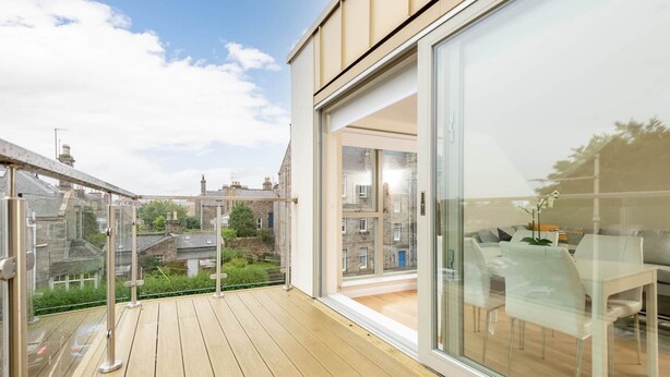 Un balcon doté d’un plancher en bois et de portes vitrées donnant sur un espace intérieur comprenant une table et des chaises.