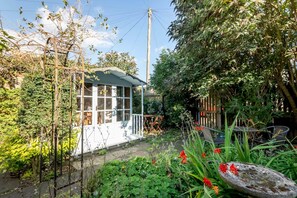 Un jardin avec un bâtiment blanc, une clôture en bois et diverses plantes.